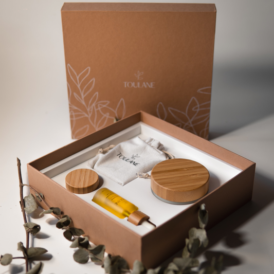 A gift set by TOLUANE, containing a face oil, beauty balm, shea butter, and a soap bar, neatly arranged in a box with compartments for each item.